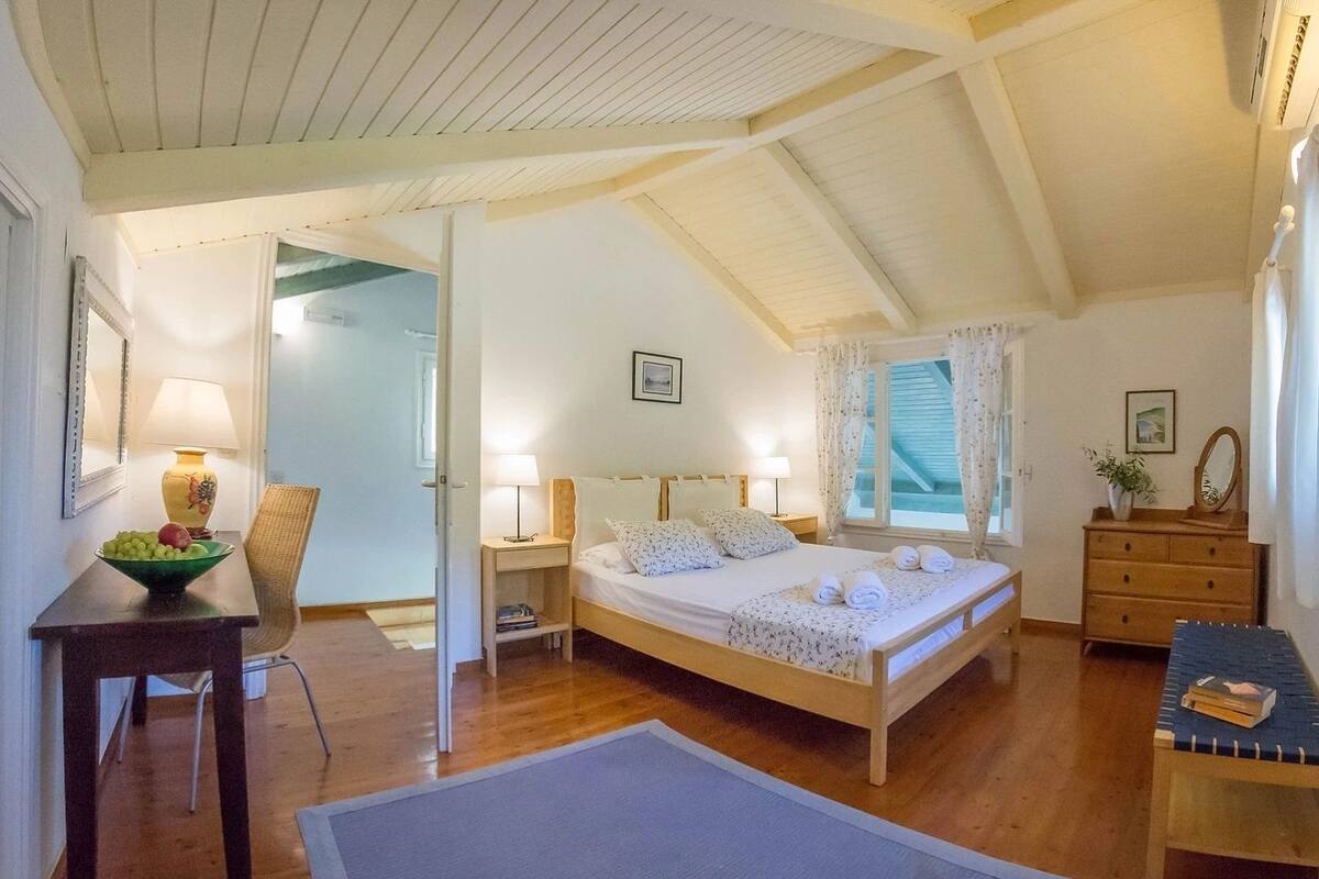 A bedroom with a wooden bed, bedside tables, a chair, and a desk with a bowl of fruit.