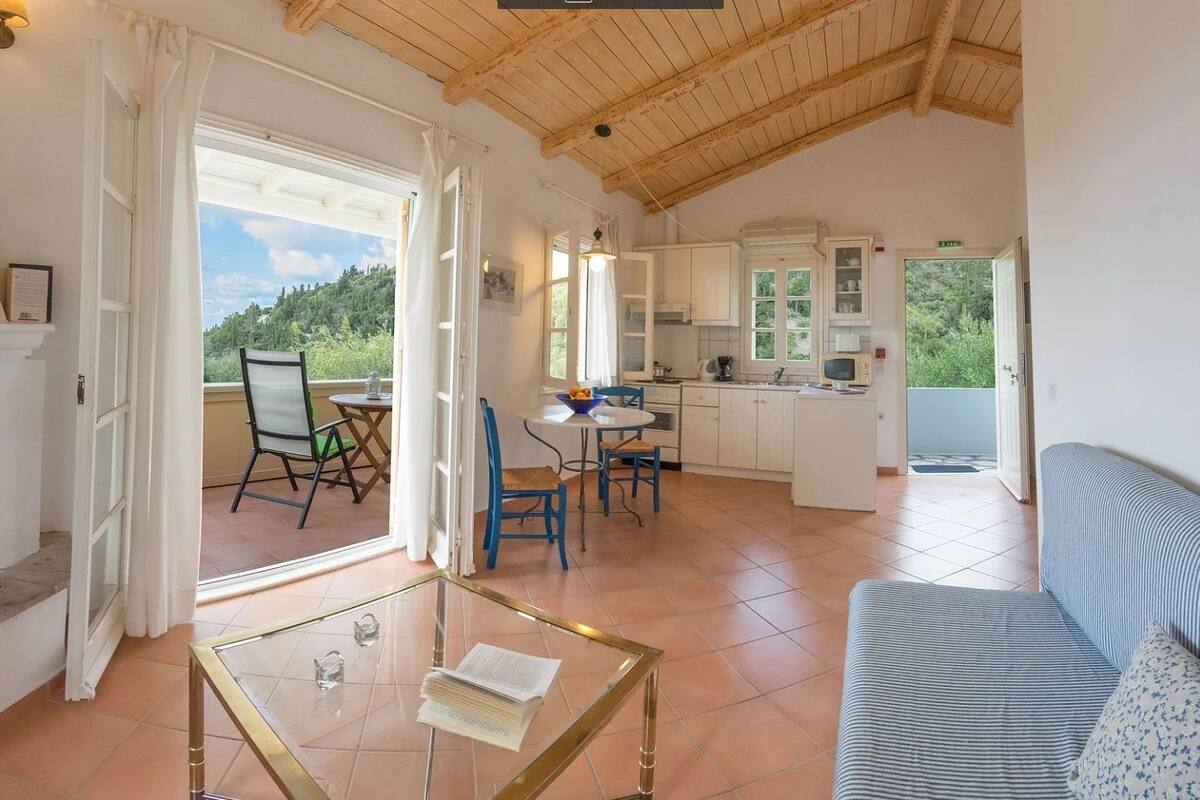 A spacious living area with a fireplace, a dining table with chairs, a kitchen area, and a balcony with a view of greenery.