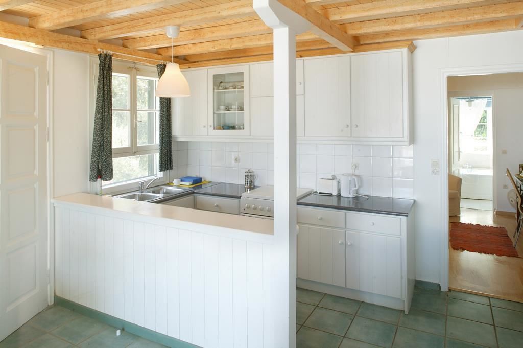Eine Küche mit weißen Schränken, Holzboden und einem Fenster mit Vorhängen.
