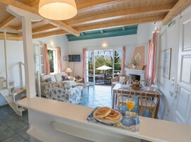 Amplia sala de estar con sofá, mesa de comedor y sillas. Cuenta con una chimenea y un televisor montado en la pared.