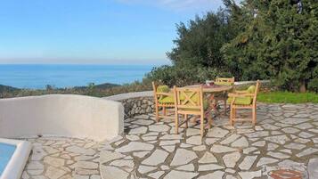 Un patio de piedra con piscina, mobiliario exterior y vistas al mar.