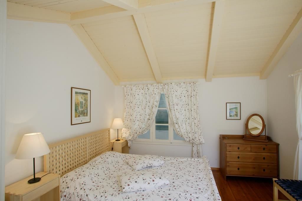 A bedroom with a bed, a nightstand, a dresser, a mirror, and a window with curtains.