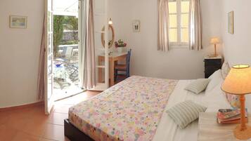 A bedroom with a bed, a desk, and a chair. There is a window with curtains and a lamp on a bedside table.