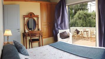 A bedroom with a bed, a dresser with a mirror, a window with curtains, and a balcony with outdoor furniture.