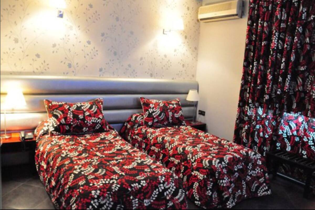A double bed with a patterned bedspread, two bedside lamps, and a wall-mounted air conditioner.