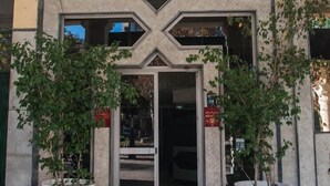 Entrada de hotel con un diseño geométrico sobre la puerta, dos plantas en macetas a cada lado y un felpudo rojo en la entrada.