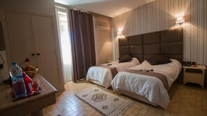 Un dormitorio con dos camas, una mesita de noche, un armario, una ventana con cortinas y una lámpara de pared.