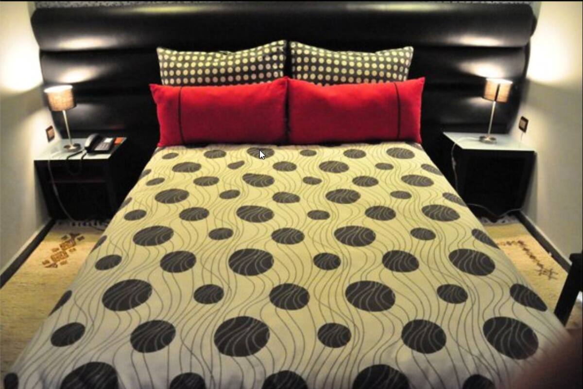 A bed with a polka dot and wavy pattern bedspread, two red pillows, and black headboard.