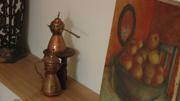Een koperen theepot en suikerpotje op een houten plank, naast een schilderij van appels in een mand.