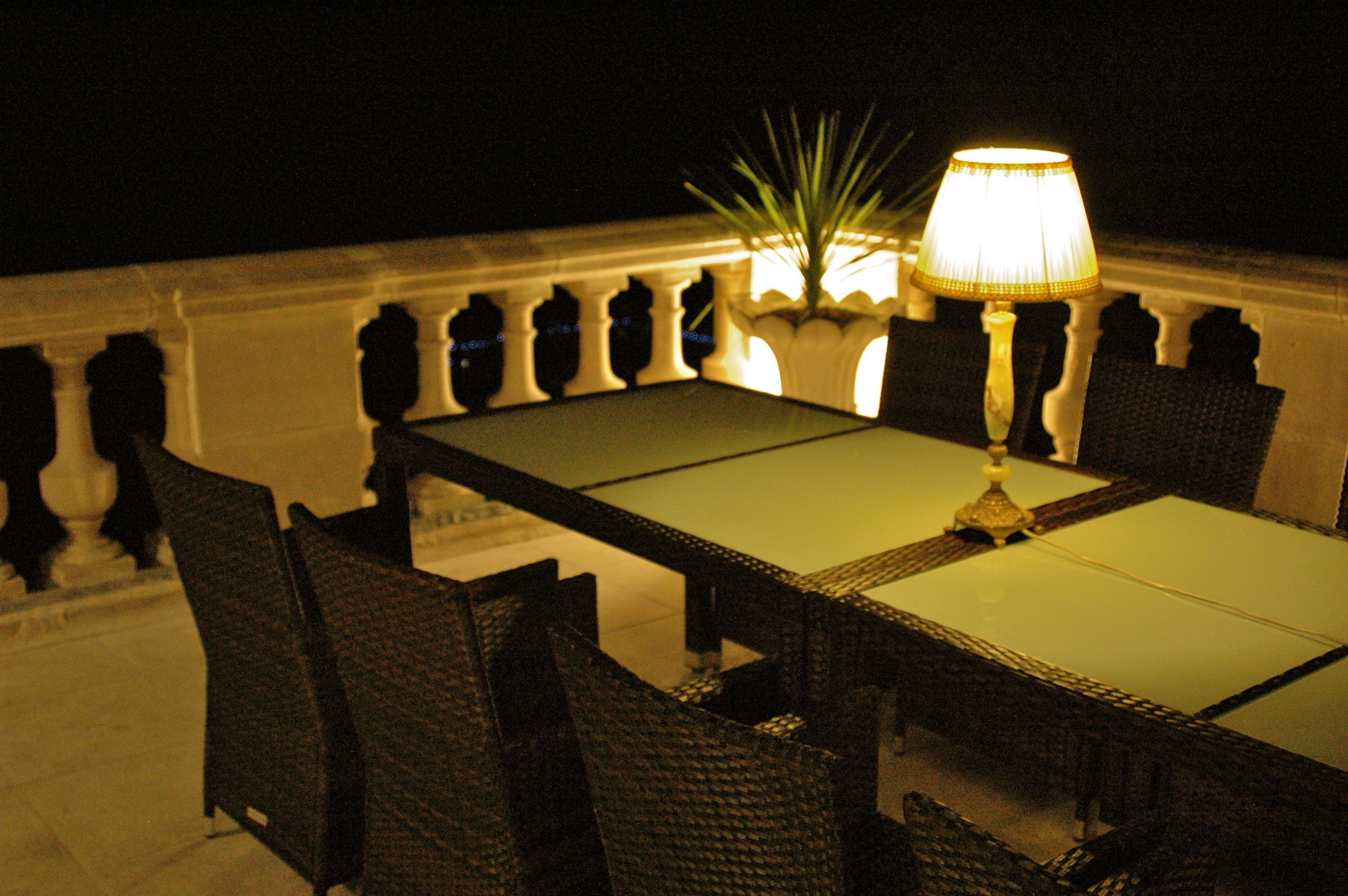 A dining table with chairs, a lamp, and a potted plant on a balcony.