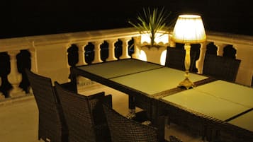 A dining table with chairs, a lamp, and a potted plant on a balcony.