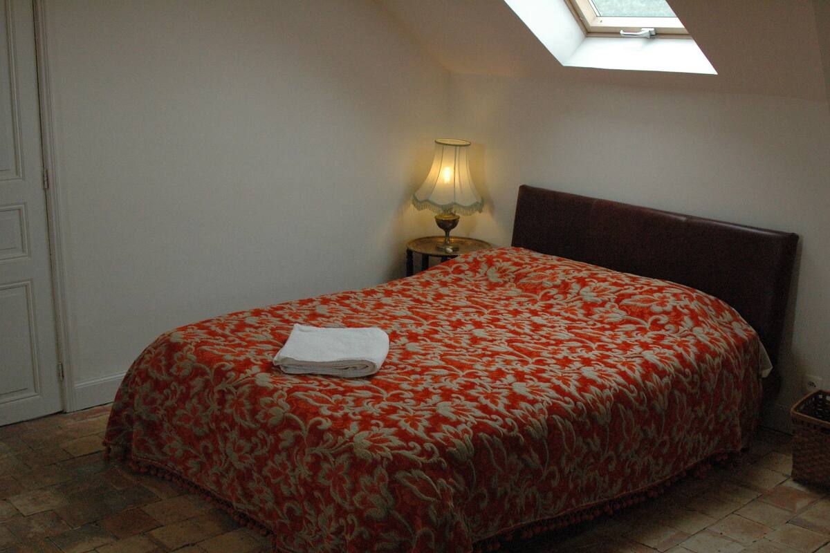 Une chambre à coucher avec un lit, une table de chevet, une lampe et une lucarne.