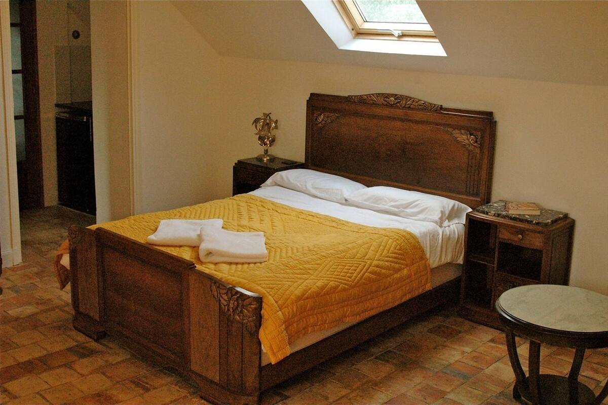 Un lit en bois avec une couette jaune, des oreillers blancs et une table de chevet avec une lampe.