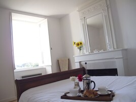 A hotel room with a bed, a tray with breakfast items, a vase with flowers, and a fireplace.