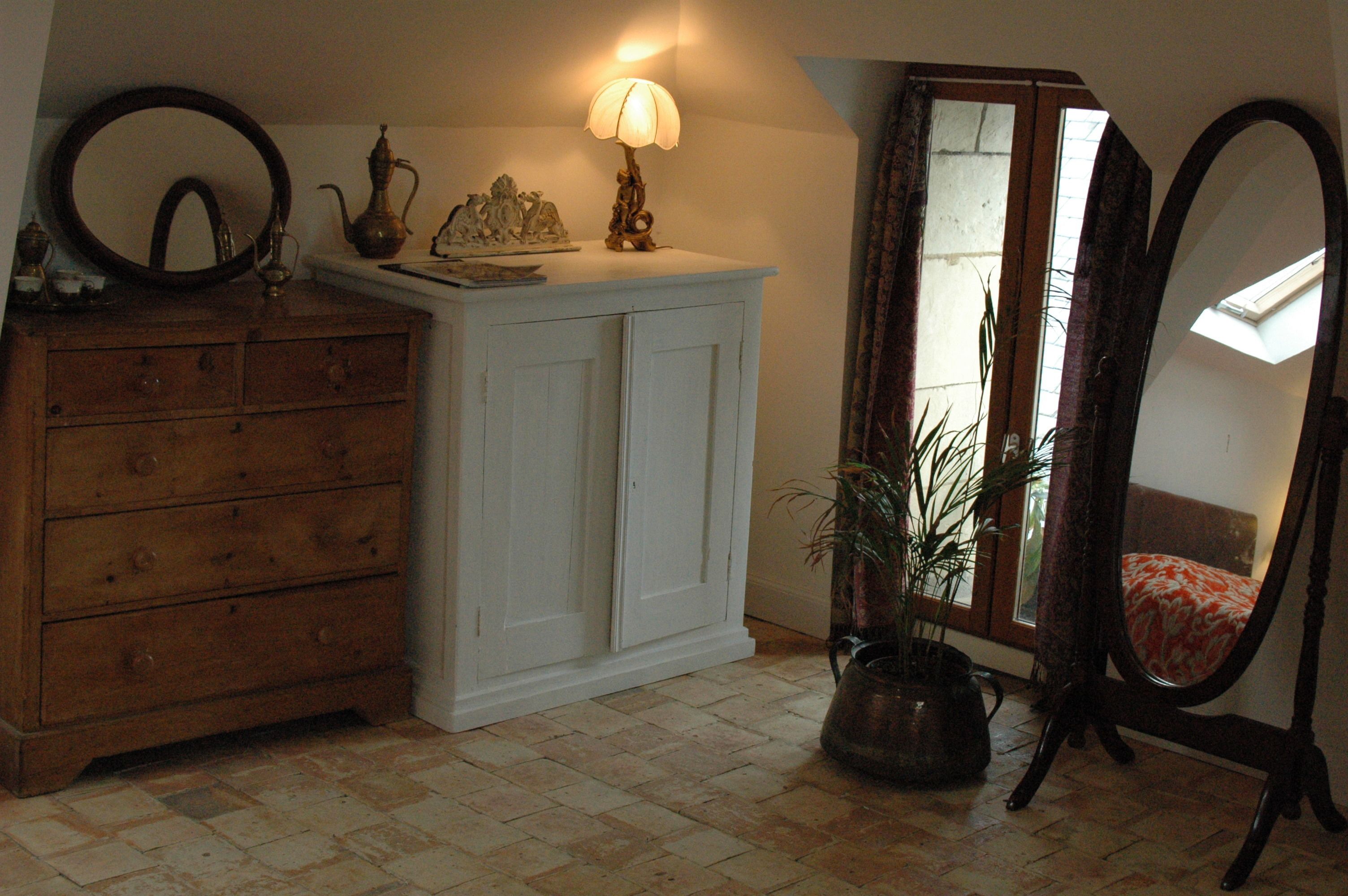 A room with a wooden dresser, a white cabinet, a lamp, a mirror, and a potted plant.