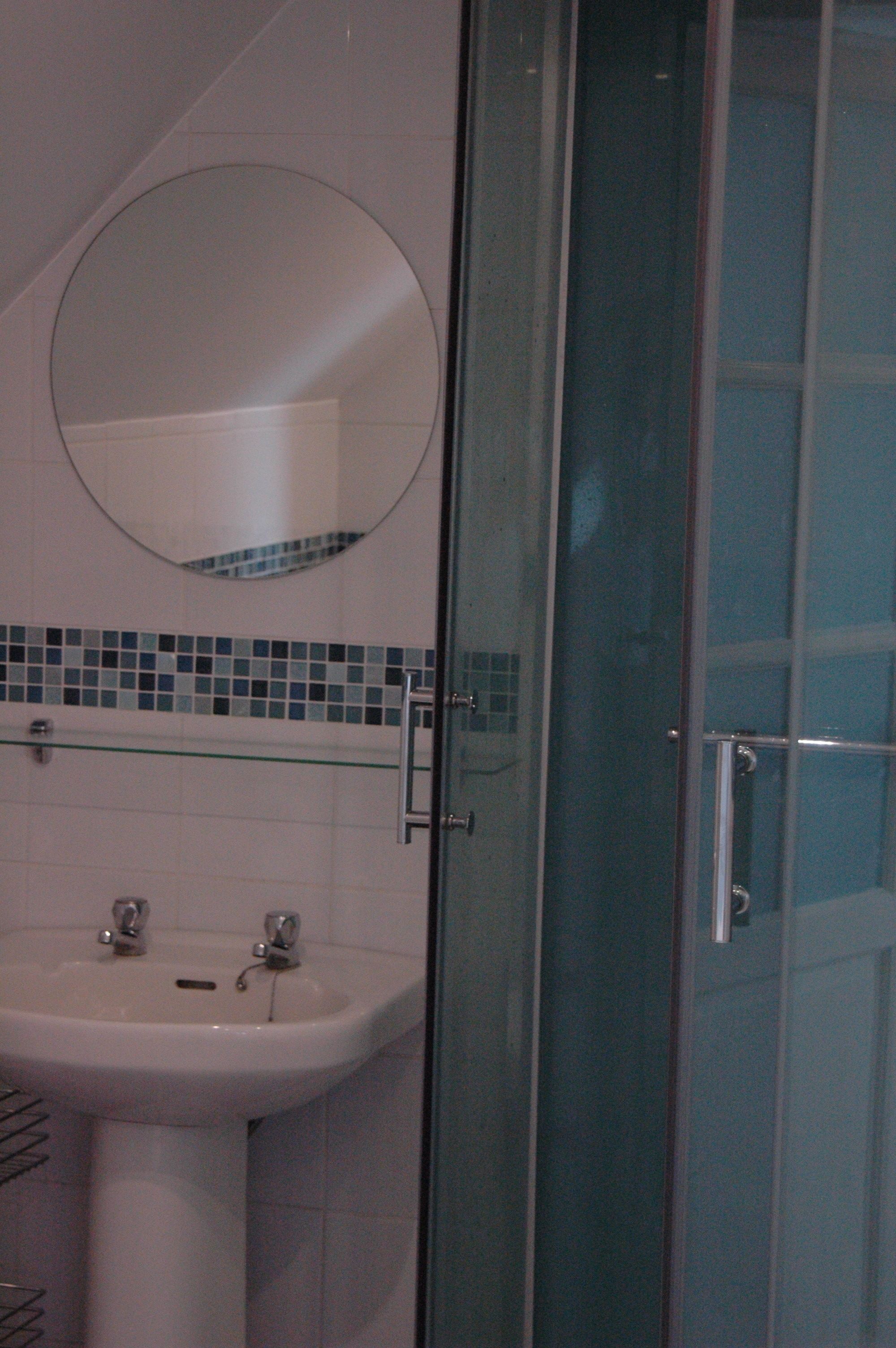 A bathroom with a glass shower enclosure, a round mirror, and a sink with a tiled backsplash.