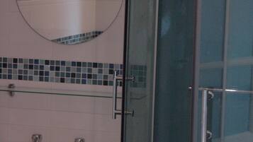 A bathroom with a glass shower enclosure, a round mirror, and a sink with a tiled backsplash.