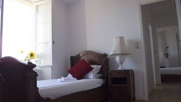 Une chambre à coucher avec un lit en bois, du linge de lit blanc, un oreiller rouge, une lampe de chevet et une fenêtre donnant sur un tournesol.