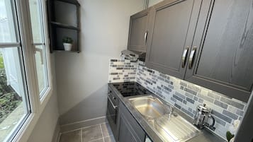 A compact kitchen with dark cabinets, a tiled backsplash, and a window providing natural light.