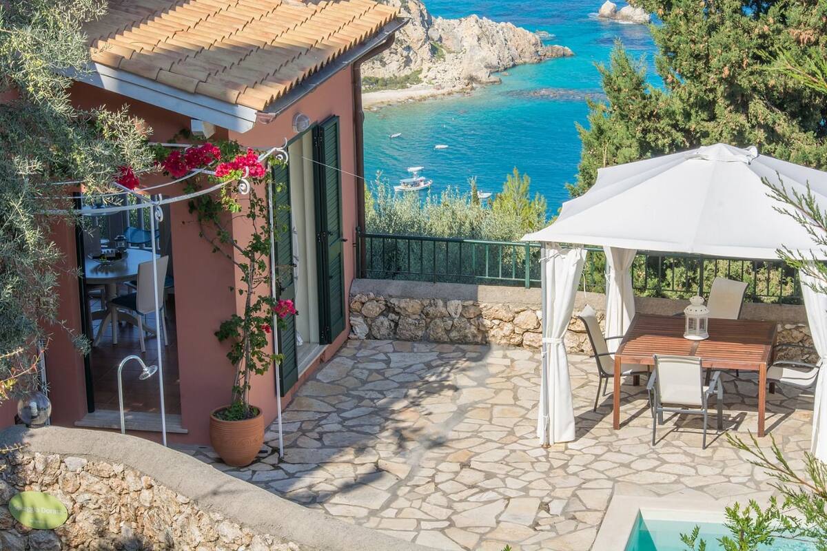 A patio with a table and chairs, a white umbrella, and a view of the sea.