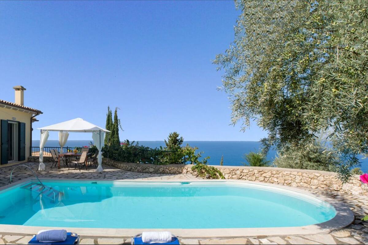 A swimming pool with lounge chairs, a covered seating area, and a view of the sea.