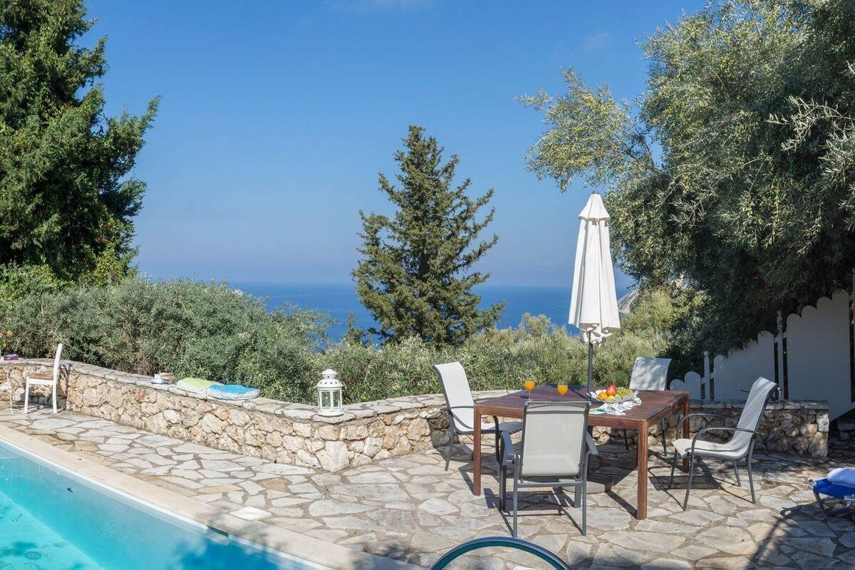 A pool with a stone deck, outdoor seating, and a view of the sea.