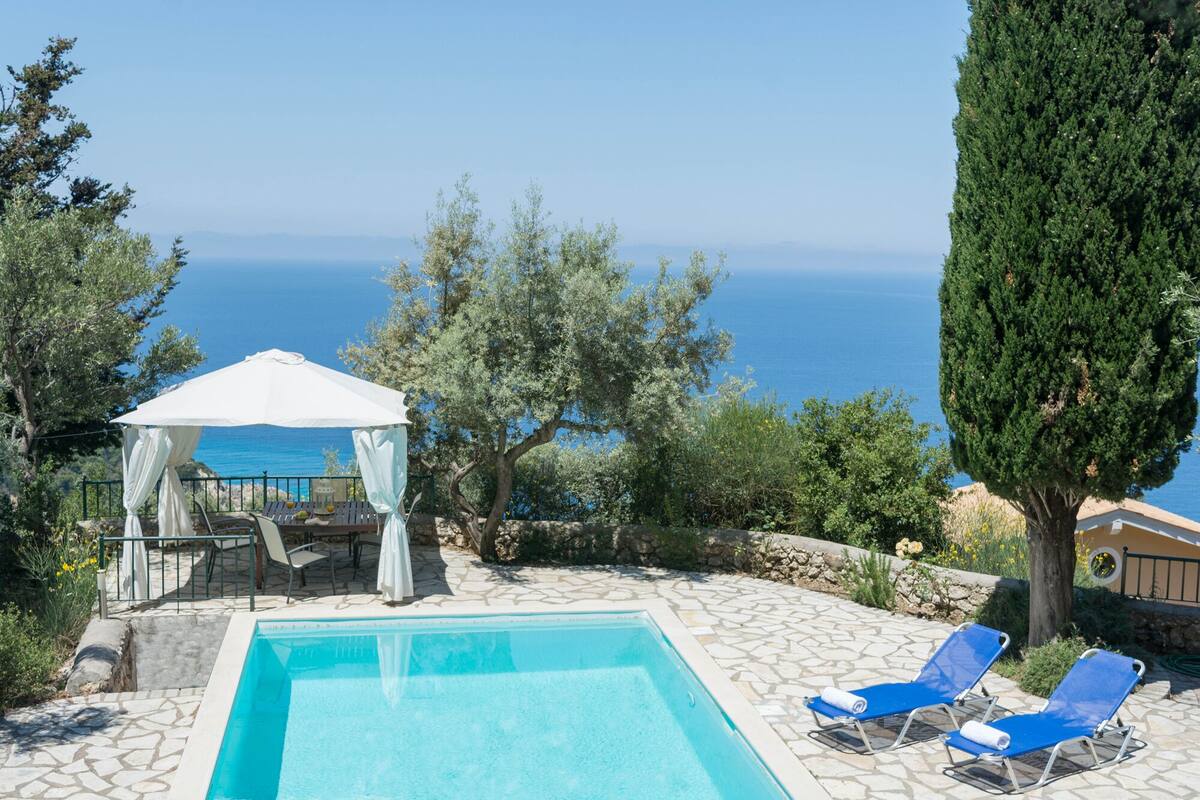 A pool area with a view of the sea, a gazebo, and lounge chairs.