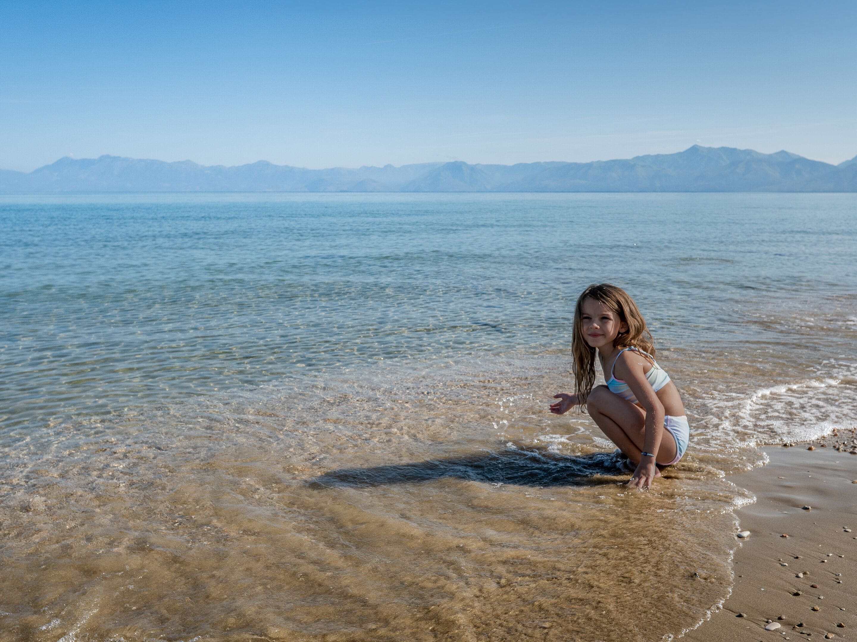 Una playa con agua cristalina y montañas al fondo.