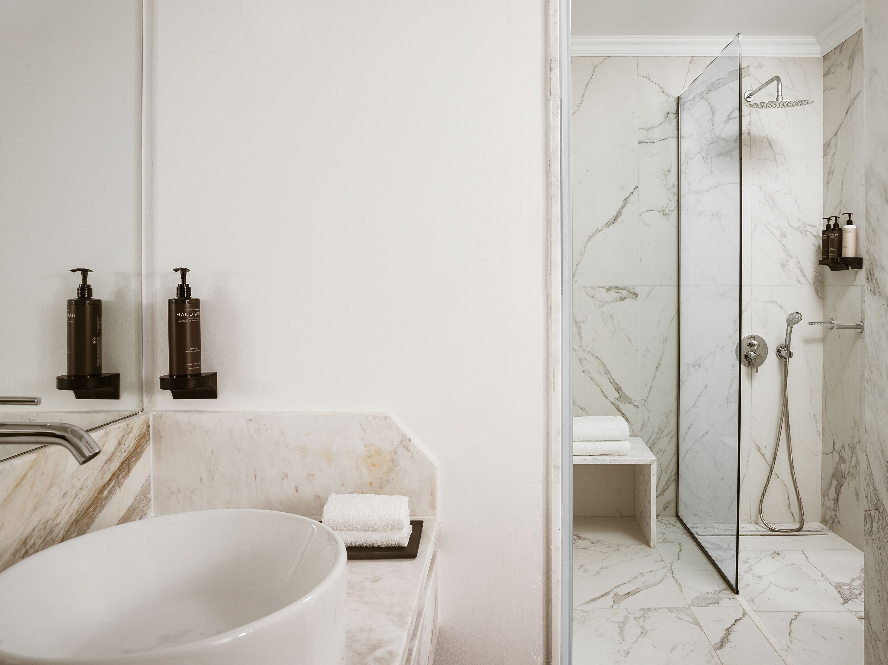 Une salle de bain avec un lavabo en marbre, une cabine de douche en verre et des articles de toilette fixés au mur.