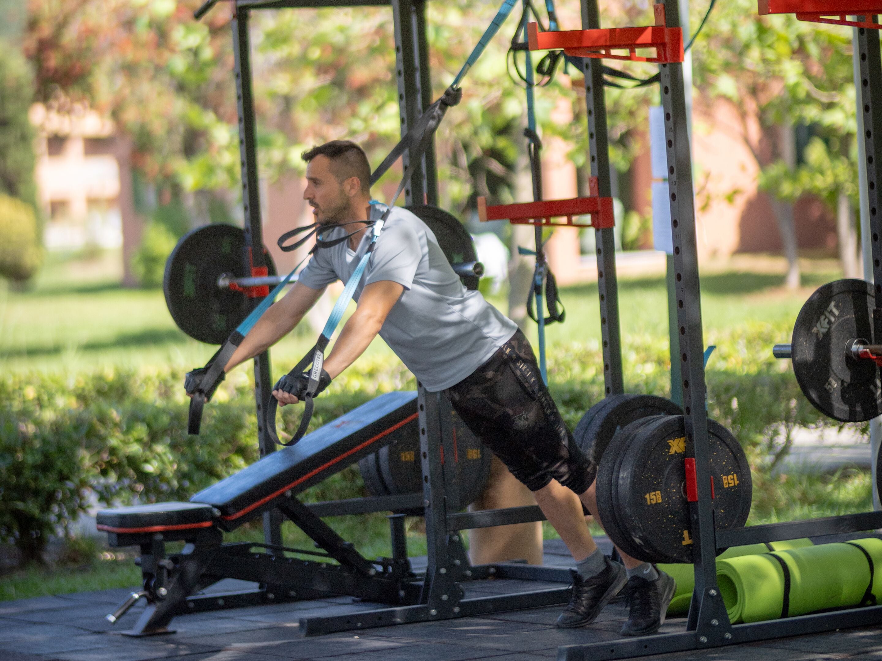 A person performing a workout using a bench press and weightlifting equipment in an outdoor setting.