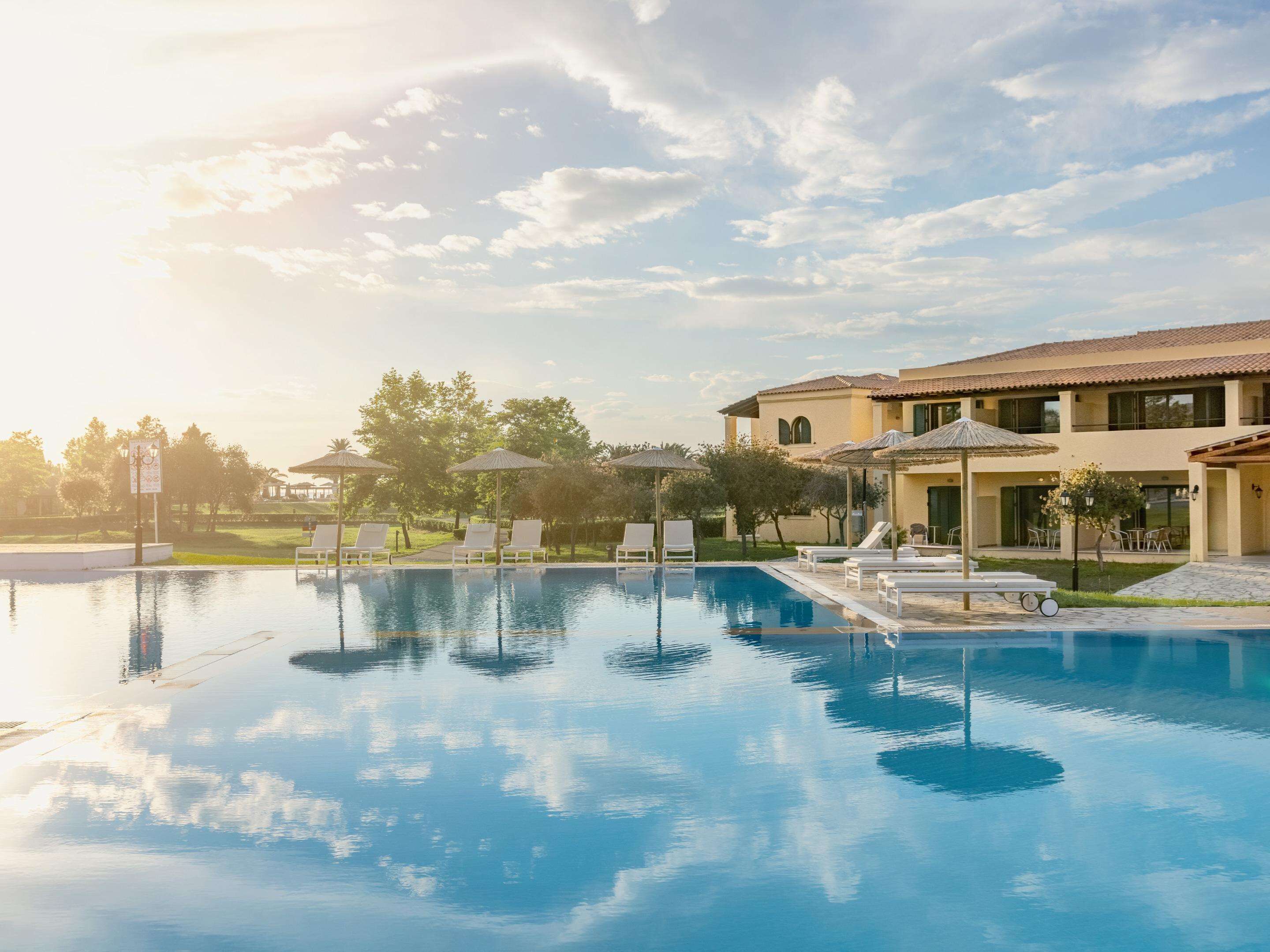 A pool area with lounge chairs and umbrellas, surrounded by a building with a tiled roof.