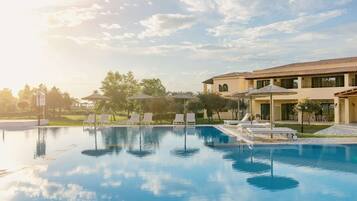 A pool area with lounge chairs and umbrellas, surrounded by a building with a tiled roof.