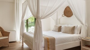 Un lit à baldaquin avec du linge de lit blanc, un panier tressé accroché au mur et une chaise en osier.