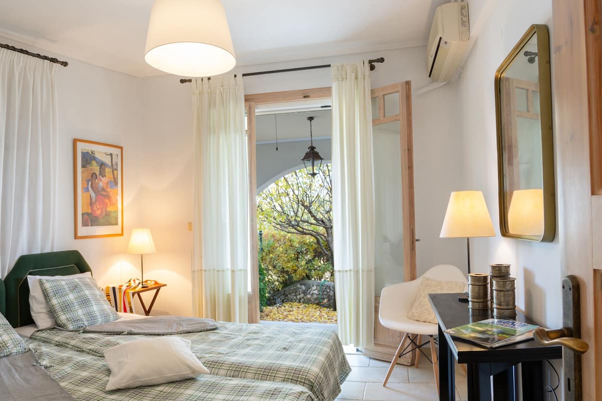 A bedroom with a bed, two bedside tables, a chair, a desk, a lamp, a mirror, and a window with curtains.