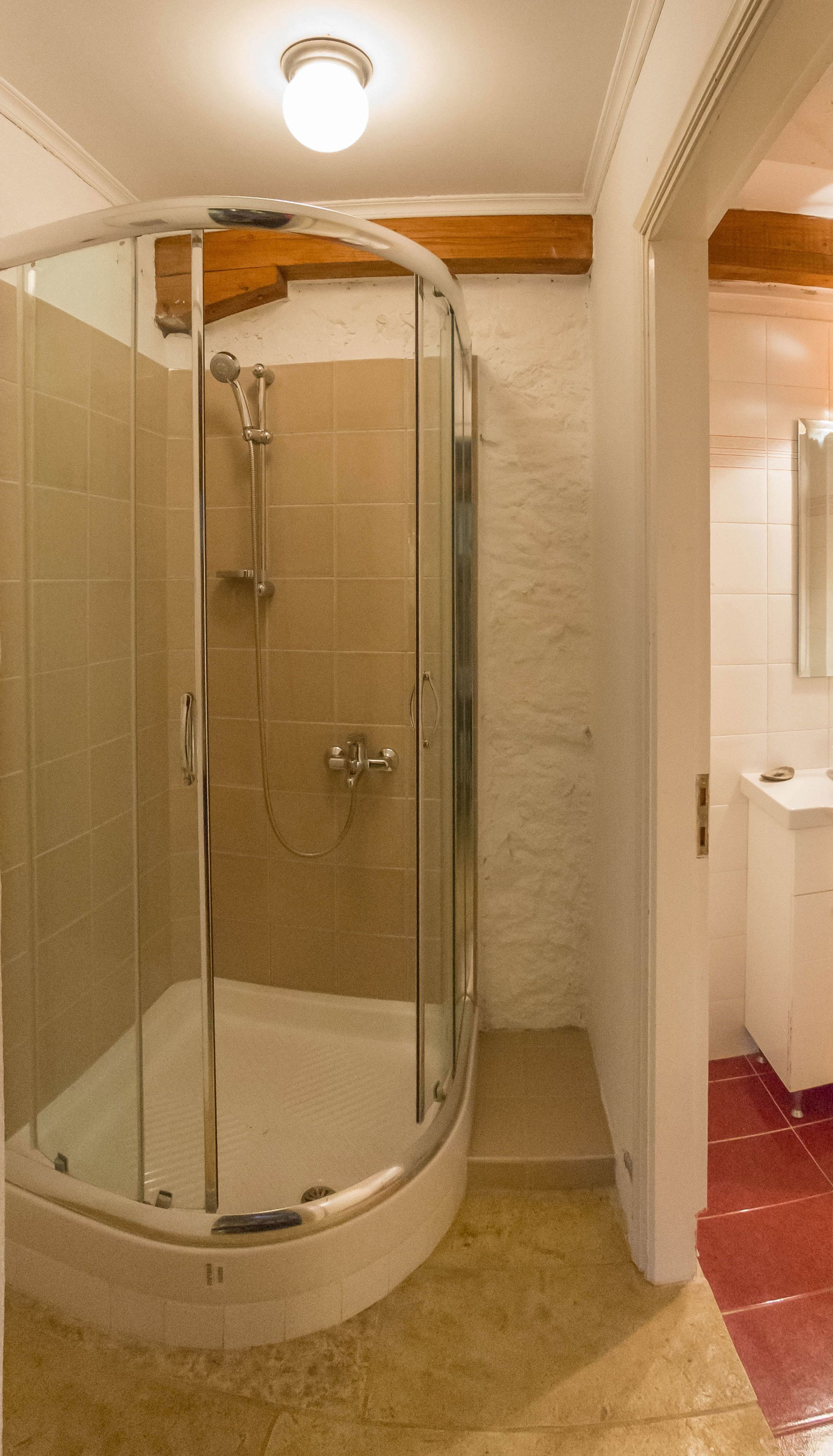 A glass-enclosed shower with a handheld showerhead and a handheld faucet.