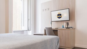 Ein Hotelzimmer mit einem Bett, einem Schreibtisch, einem Sessel, einem an der Wand befestigten Fernseher und einem Fenster.