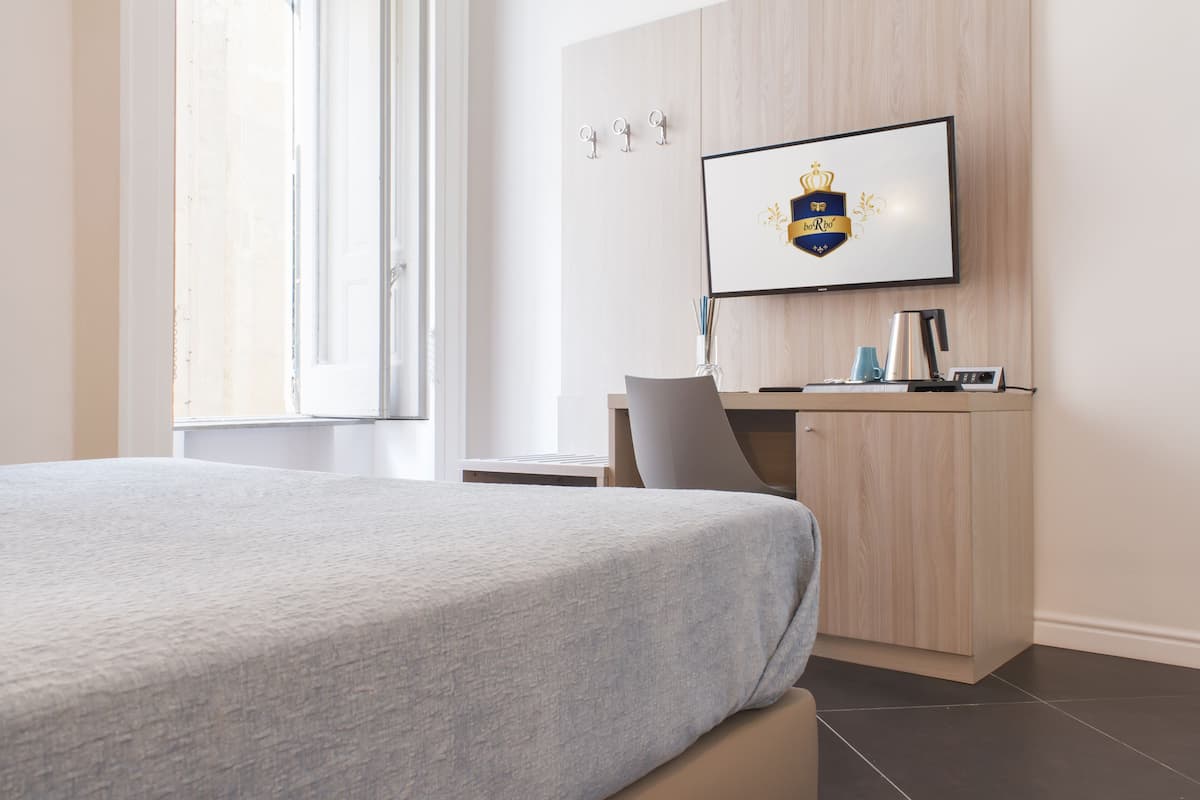 Habitación de hotel con cama, escritorio, silla, televisor montado en la pared y ventana.