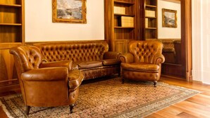 Ein Zimmer mit einem braunen Ledersofa, zwei Sesseln, Holzregalen und gerahmten Kunstwerken an den Wänden.