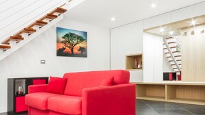Ein modernes Wohnzimmer mit einem roten Sofa, einer Holztreppe und einem Bild von Baum und Elefant.