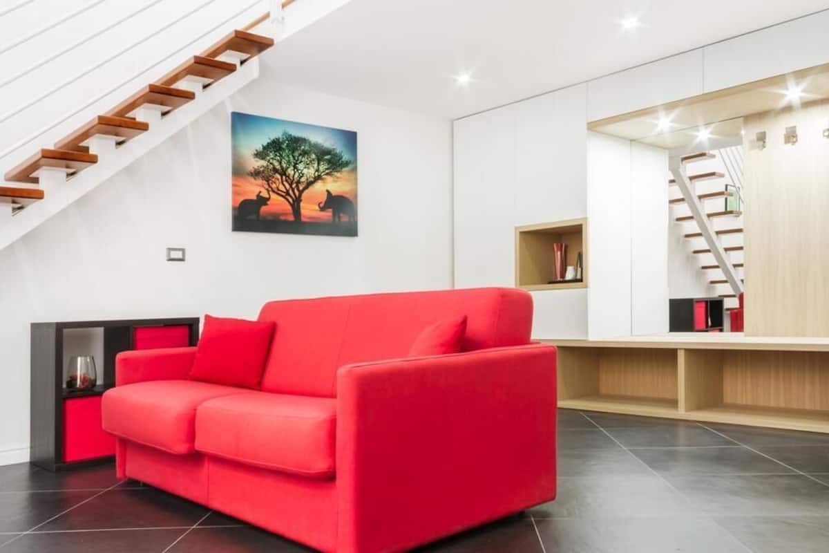 Una sala de estar moderna con un sofá rojo, una escalera de madera y un cuadro con un árbol y un elefante.