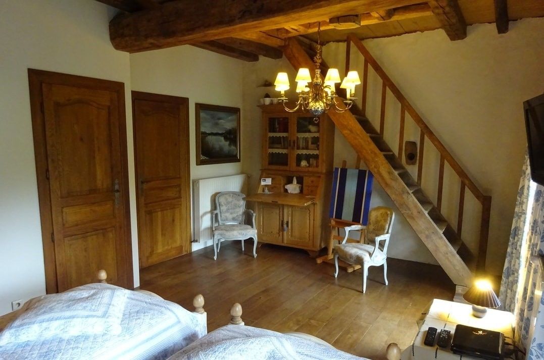A rustic room with wooden beams, a staircase, a chandelier, and a bed with patterned bedding.