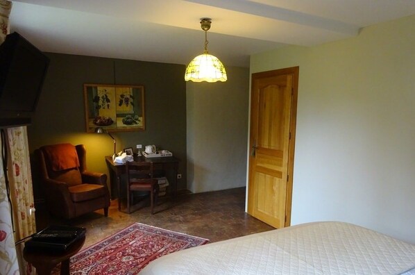 Un dormitorio con una cama, una puerta de madera, un escritorio con lámpara, una silla y un cuadro en la pared.