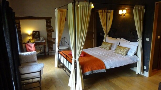 Une chambre à coucher avec un lit à baldaquin, un bureau avec une chaise et un escalier menant à un niveau supérieur.
