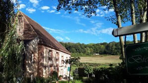 Un bâtiment rustique en briques, doté d’un toit en pente, entouré d’une végétation luxuriante et d’une pelouse bien entretenue.