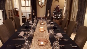 Une longue table à manger, décorée de bougies, de verres et de couverts en argent, entourée de chaises.