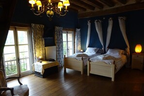A bedroom with a double bed, a bedside table, a chair, a chandelier, and a window with curtains. - Moulin de Sévoux (Longny les Villages)