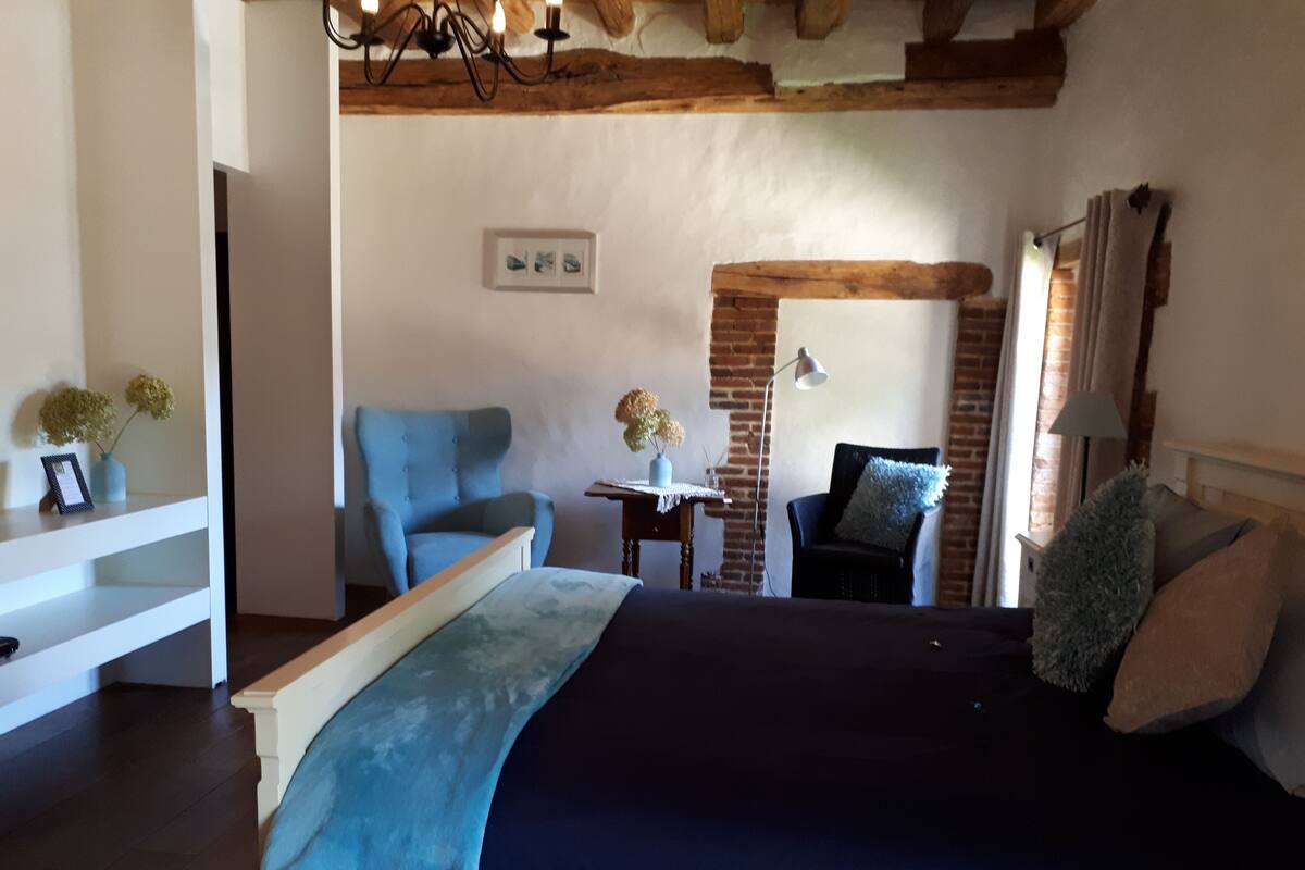 A bedroom with a bed, two chairs, a small table, and a lamp.