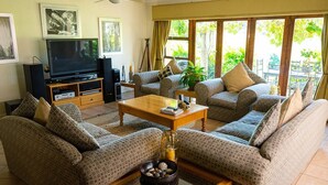 A living room with patterned sofas, a wooden coffee table, a television, and a large window with a view of greenery. - Stockowners Farm House (Howick)