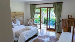 A bedroom with a large bed, a wooden headboard, a chair, a wooden cabinet, and a sliding glass door leading to a balcony. - Stockowners Farm House (Howick)