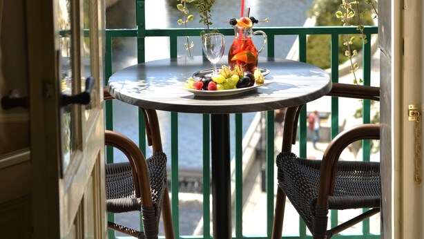 Un balcon avec une table dressée pour deux personnes, donnant sur une rivière et des bâtiments aux couleurs vives.